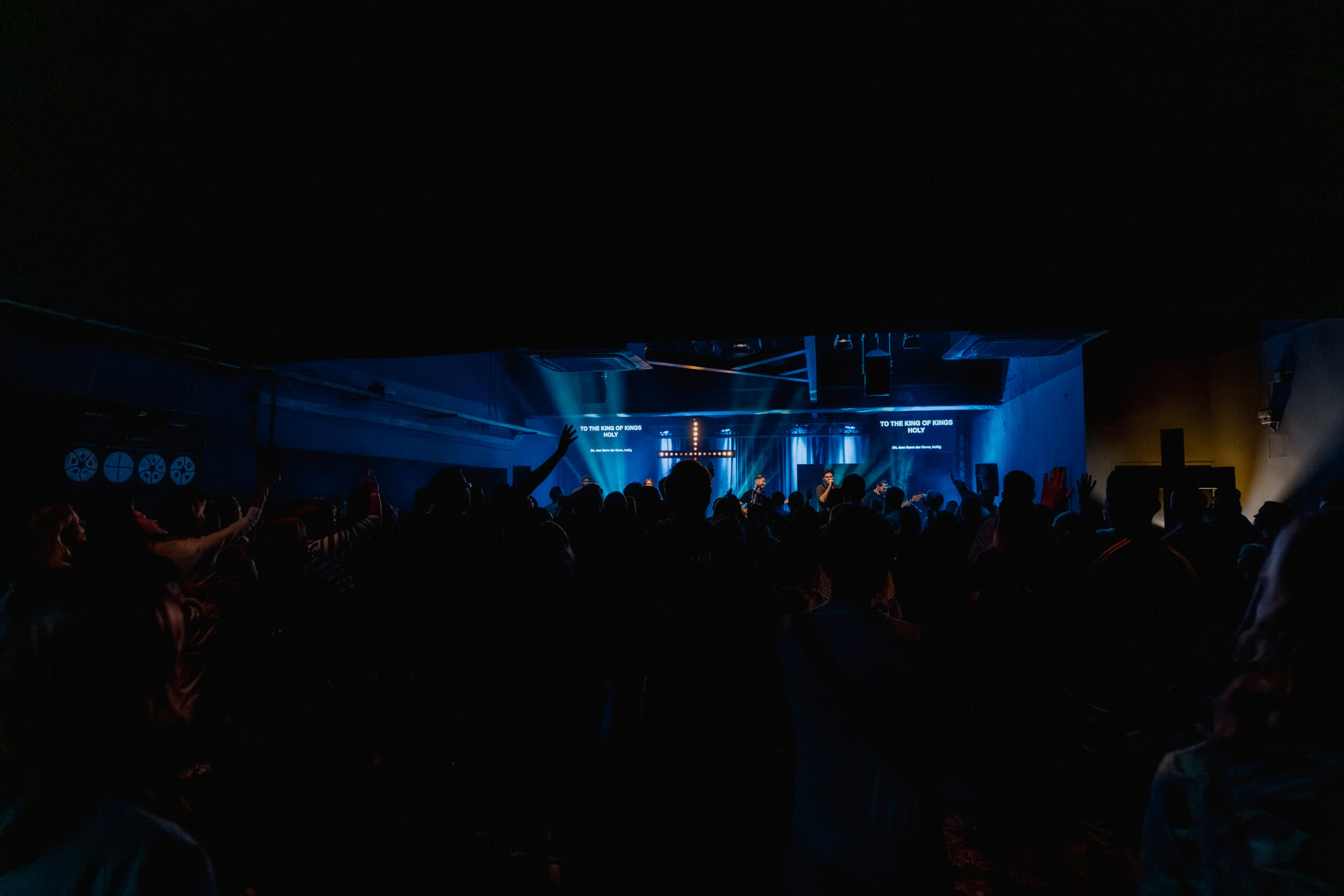 Dunkler Konzertsaal mit Bühne, blauer Beleuchtung und Publikum im Vordergrund.