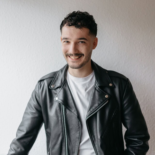Ein junger Mann mit dunklen, kurzen Haaren trägt eine schwarze Lederjacke und ein weißes T-Shirt, er.