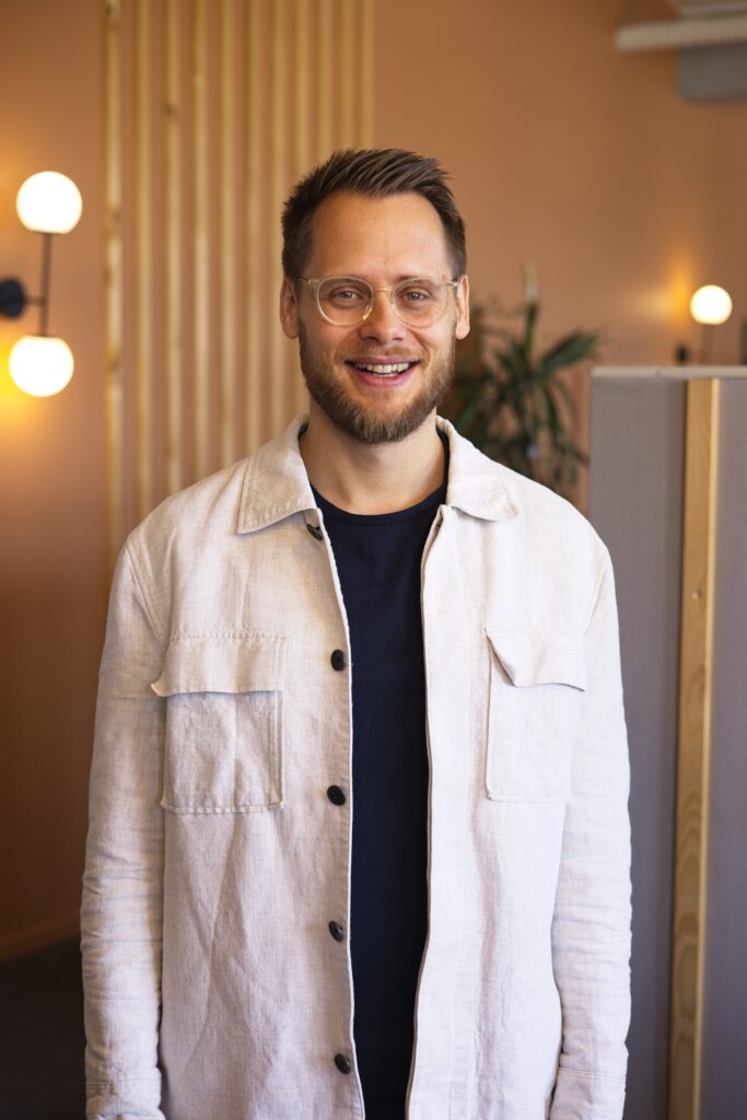 Lächelnder Mann mit Brille und Bart in modernem Raum, repräsentiert die offene Gemeinschaft der ICF Basel Kirche.
