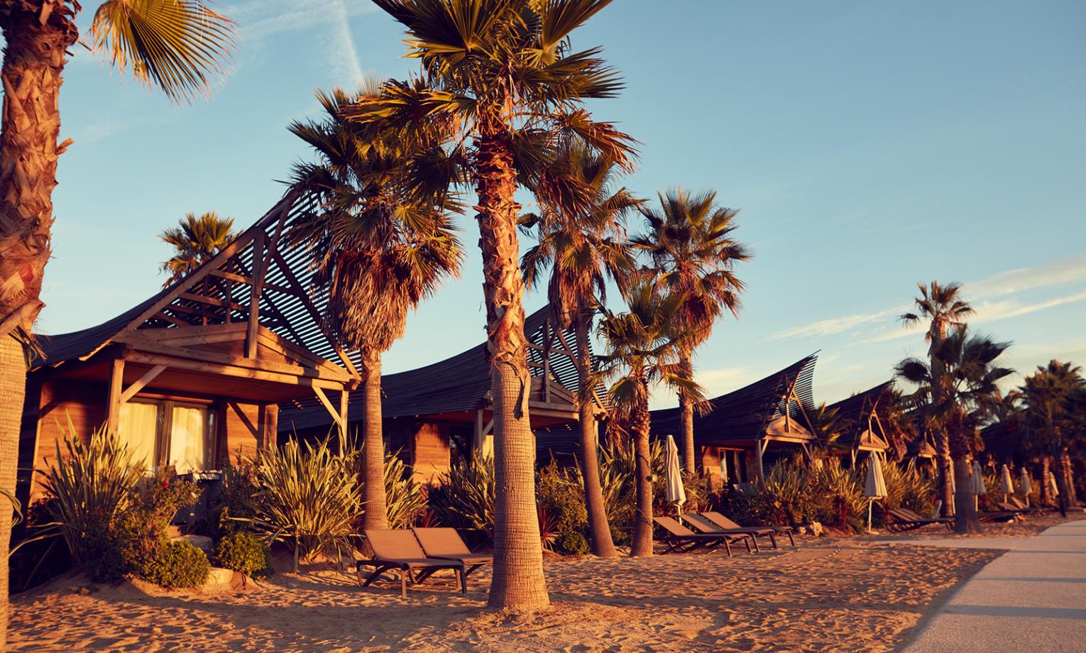 Entspannte Strandlandschaft mit Palmen, Liegestühlen und Strandhütten bei Sonnenuntergang, ideal für das Herbstcamp.