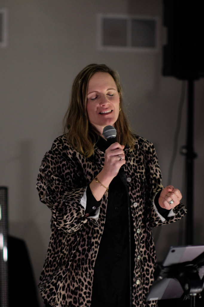 Frau singt mit Mikrofon, trägt Leo-Musterjacke, steht vor einem Mikrofon.