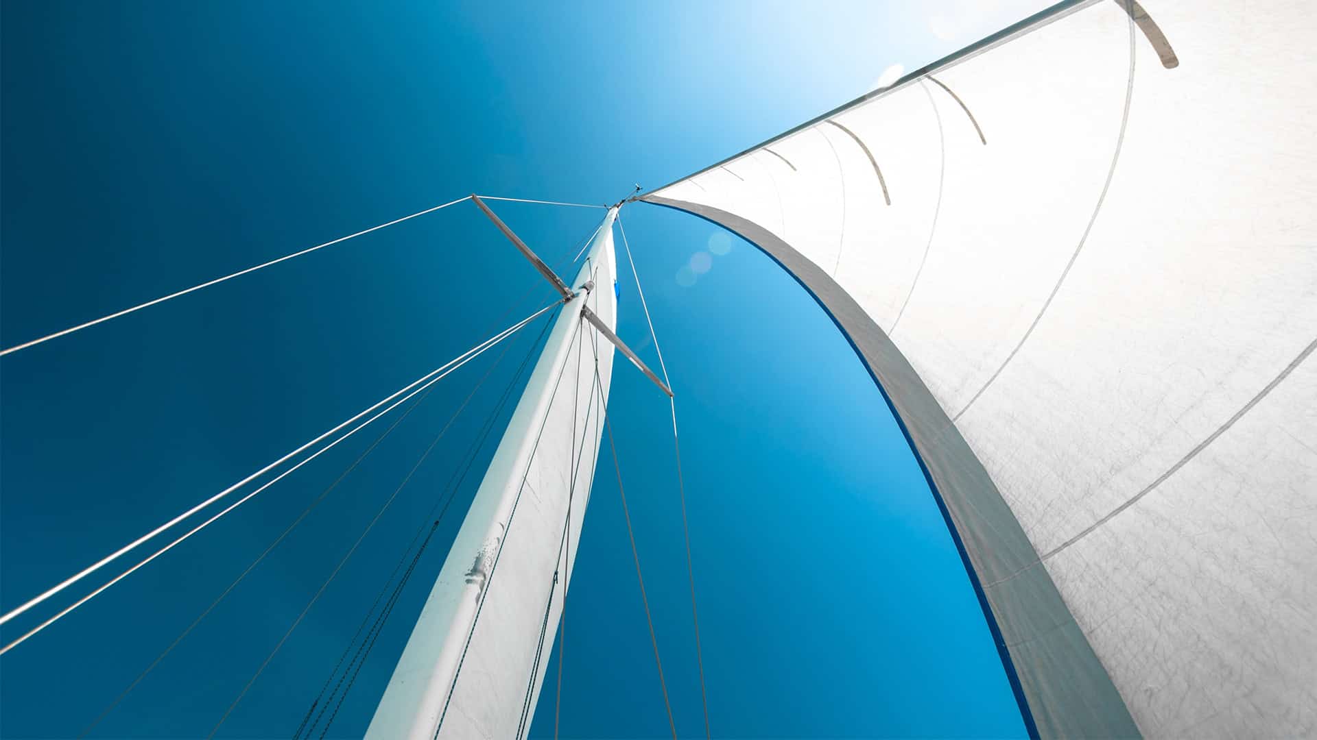 An upward view of a sailing boat with white sails against a blue sky symbolizes freedom, adventure and community in a Christian context.