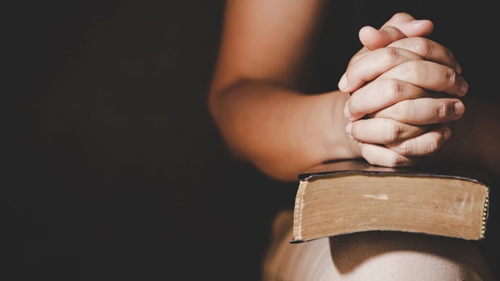 Gebetshände ruhen auf einem Gebetsbuch, Symbol für Glauben und spiritualuelle Verbindung in der Kirche.
