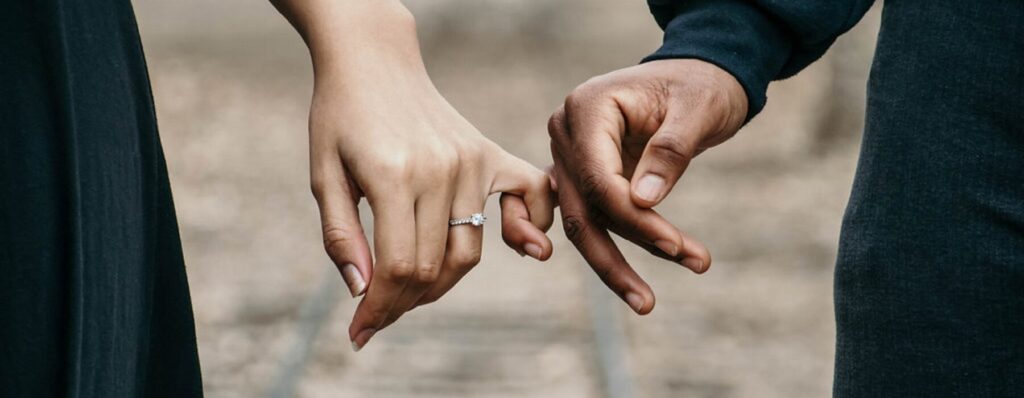 Detailaufnahme eines verlobten Paares, das sich die Hände hält, mit einem Diamantring an der Hand der Frau, Symbol für Liebe und Zusammenhalt, bei ICF Mannheim.