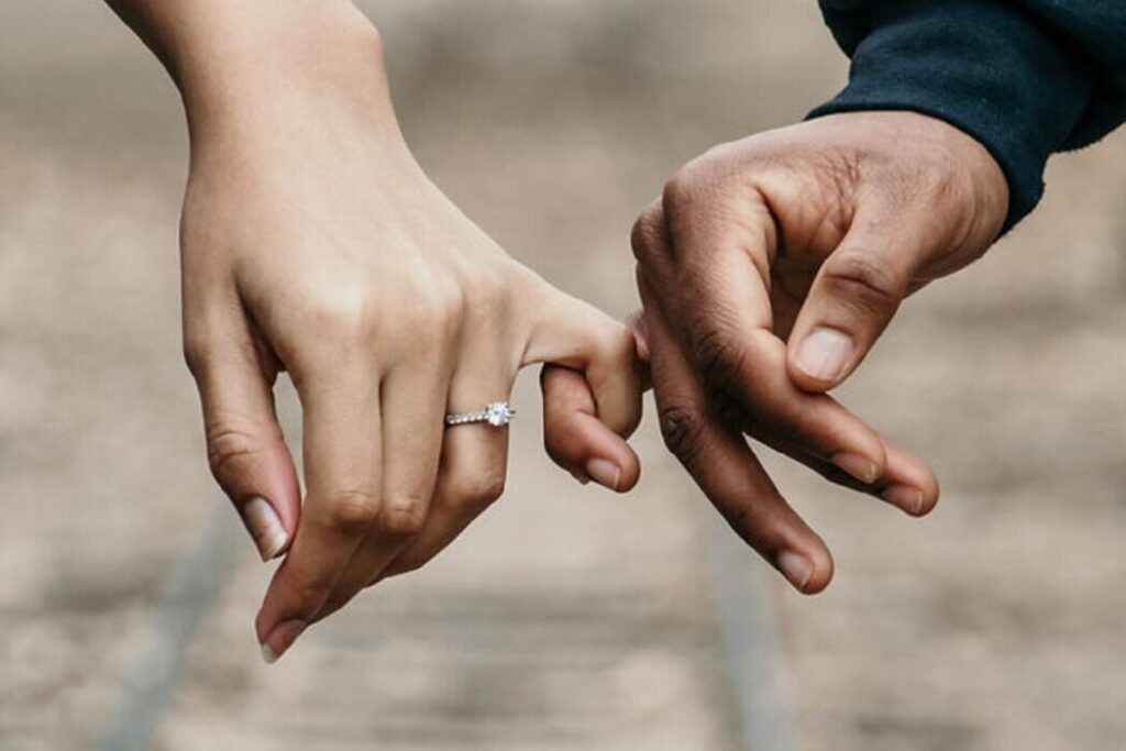 Hände halten sich liebevoll an den Fingern mit Ehering, Symbol für Liebe und Zusammenhalt.