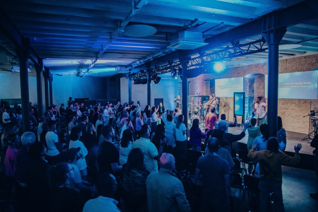 Gemeinde beim Gottesdienst in Mannheim mit Live-Band und Gebet, Menschen engagieren sich aktiv im Glauben, moderner Kirchenraum, inspirierende Atmosphäre.