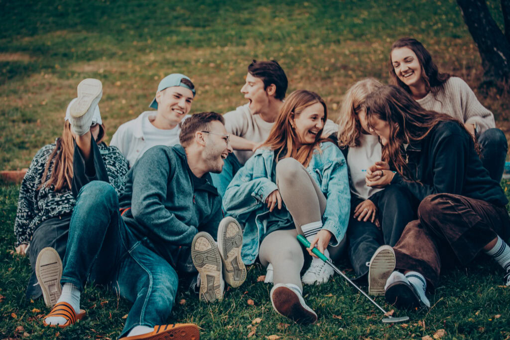 Lachen, Spaß und Gemeinschaft bei einem Outdoor-Treffen der Jugendlichen im Park, umgeben von Natur und Herbstblättern. Eine lebendige Szene der sozialen Interaktion und Freude unter jungen Menschen.